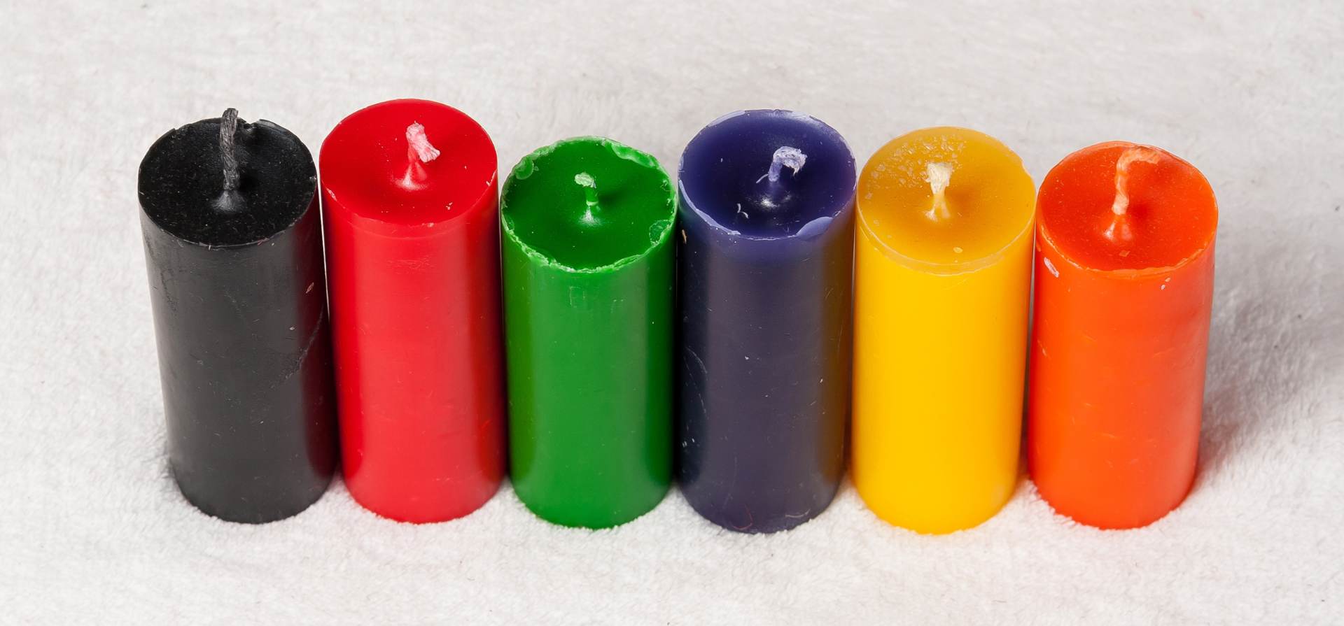 Ein Holztisch, auf dem viele bunte Kerzen in verschiedenen Größen und Farben angeordnet sind.