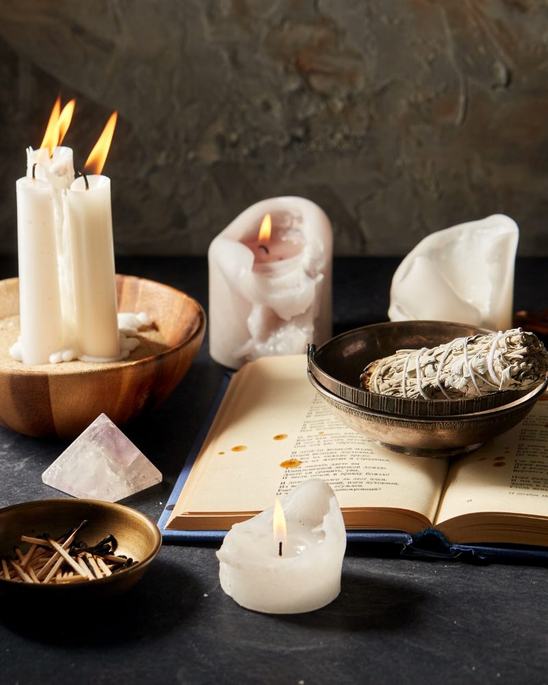 Ein brennendes Salbeibündel und eine leuchtende Kerze auf einem spirituellen Altar, umgeben von sanftem Licht.